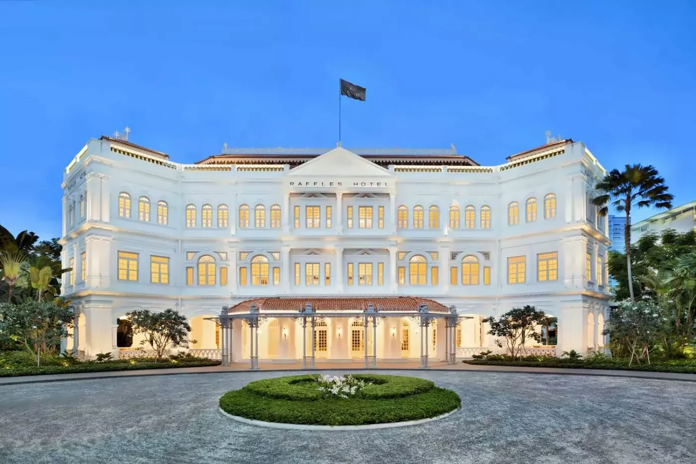 Illuminated white facade and entrance of Raffles Singapore at dusk