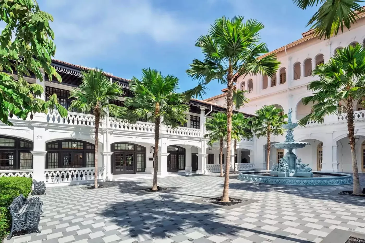 Palm-lined courtyard and fountain beside the white verandahs of Raffles Singapore