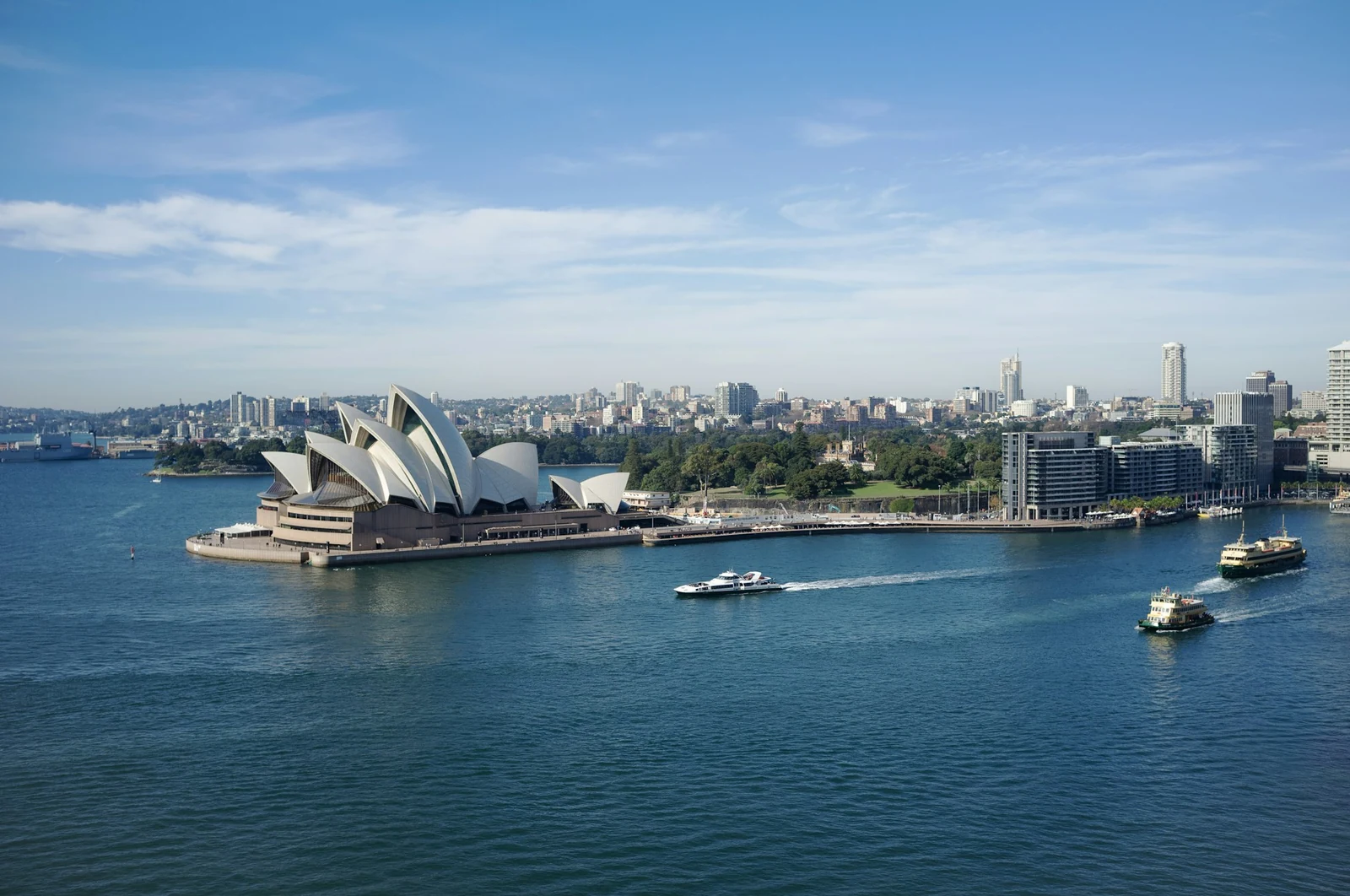 Ferries pass the Sydney Opera House with the Royal Botanic Garden behind it